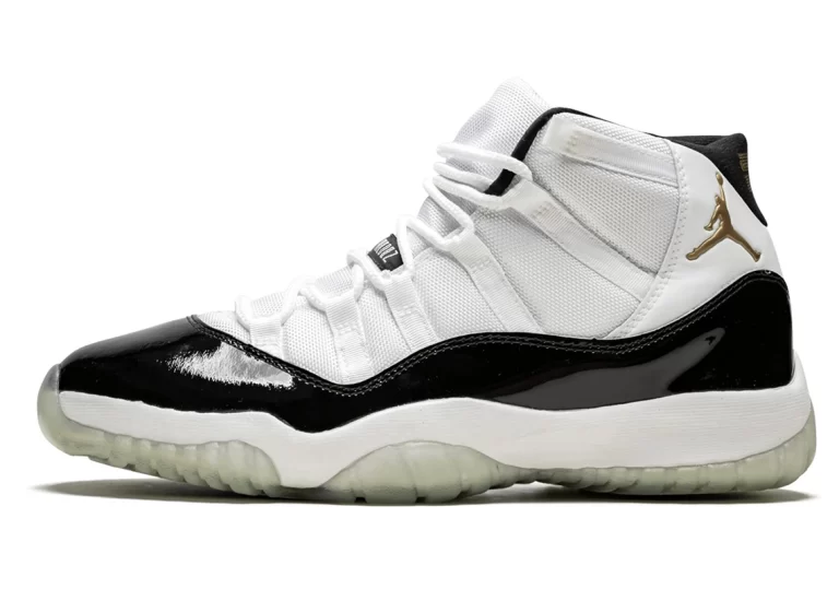 Image of the Air Jordan 11 Retro DMP sneakers with a sleek black and white colorway, metallic gold accents, patent leather, mesh, and textured leather construction, and a translucent outsole with a pre-aged white midsole. The image shows the sneakers from a side view, with the toe box and heel visible.