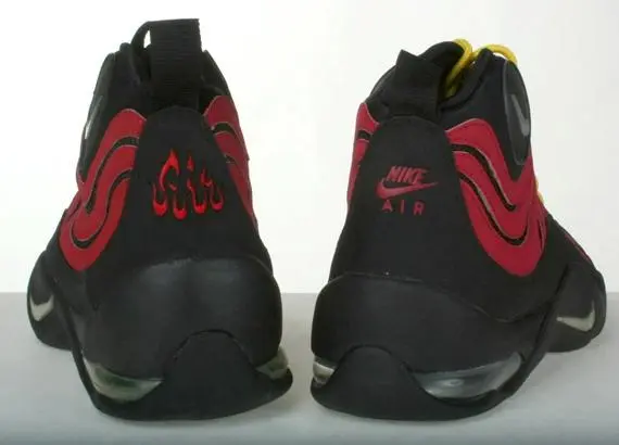 The back of the shoe features a black heel with a large Nike logo and a red stripe running down the center. The ankle collar is padded and black, with a white Nike Air logo on the back. The midsole is white with black and red accents, and the outsole is black with a red Nike logo.
