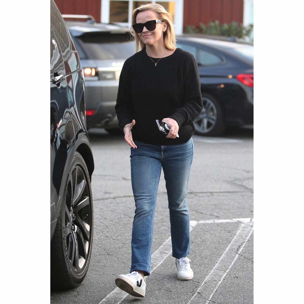 Reese Witherspoon wearing Veja sneakers with black fabric upper and white sole, featuring Veja's signature 'V' logo and made with eco-friendly materials.