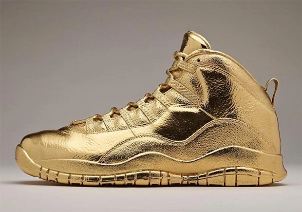 Image of gold-colored Air Jordan sneakers with the OVO (October's Very Own) logo on the tongue and gold laces. The shoes are resting on a white background.