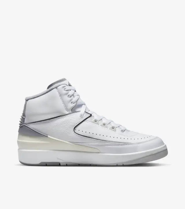 Air Jordan 2 'Cement Grey' sneakers with white leather upper, cement grey accents on the tongue, Air Jordan branding, and heel, black piping outlining the panels, sail heel counter, grey rubber outsole, and city skyline-inspired insoles with the quote 'Look, up in the air.'