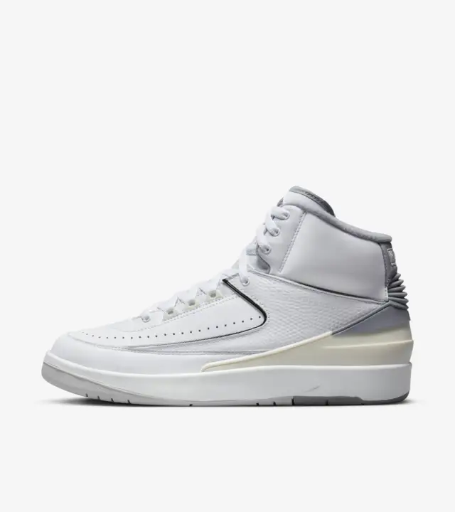 Lateral side - Air Jordan 2 'Cement Grey' sneakers with white leather upper, cement grey accents on the tongue, Air Jordan branding, and heel, black piping outlining the panels, sail heel counter, grey rubber outsole, and city skyline-inspired insoles with the quote 'Look, up in the air.'