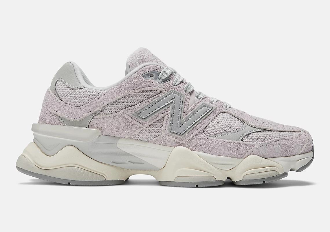 Image showcasing the New Balance 9060 sneakers in the "December Sky" colorway. Muted pink and gray hues with off-white and concrete accents, featuring a shaggy suede overlay and a distinctive diamond-shaped outsole pattern.