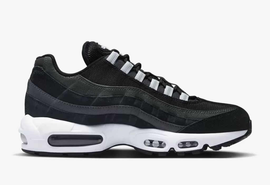 A close-up photo of an all-black Nike Air Max 95 sneaker. The sneaker has a black mesh upper with black suede accents on the mudguard and heel. The Nike Air logo is embroidered on the tongue and heel in black. The midsole is white and the outsole is black.